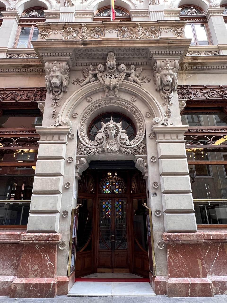 Ornate carved stone doorway of the Real Casino de Murcia on Calle Trapería, with lion heads, a female bust above the arch and a wooden door with stained glass