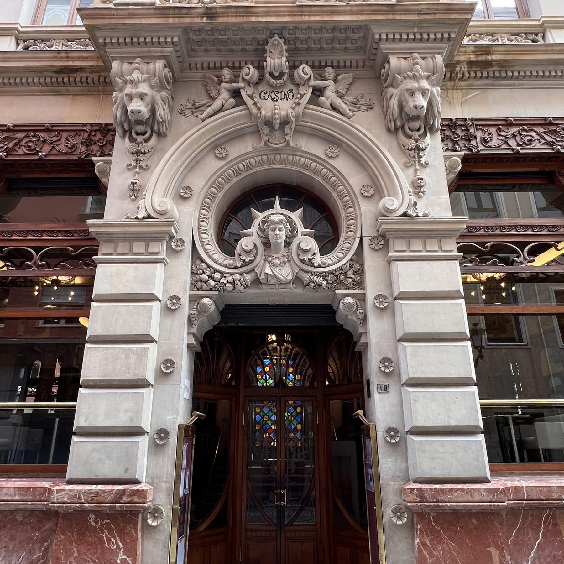 Ornate carved stone doorway of the Real Casino de Murcia on Calle Trapería, with lion heads, a female bust above the arch and a wooden door with stained glass